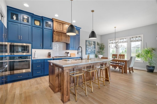 15297 W 172nd Pl, Olathe, KS 66062 - kitchen with stainless steel appliances, light wood-style flooring, blue cabinetry, a breakfast bar, and backsplash