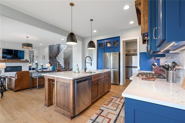 15297 W 172nd Pl, Olathe, KS 66062 - kitchen featuring stainless steel appliances, blue cabinetry, light wood-style flooring, a large fireplace, and glass insert cabinets