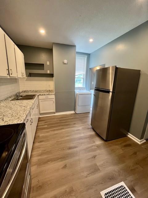 2022 Jules St, Saint Joseph, MO 64501 - kitchen with stainless steel appliances, white cabinetry, washing machine and dryer, light wood-style floors, and backsplash