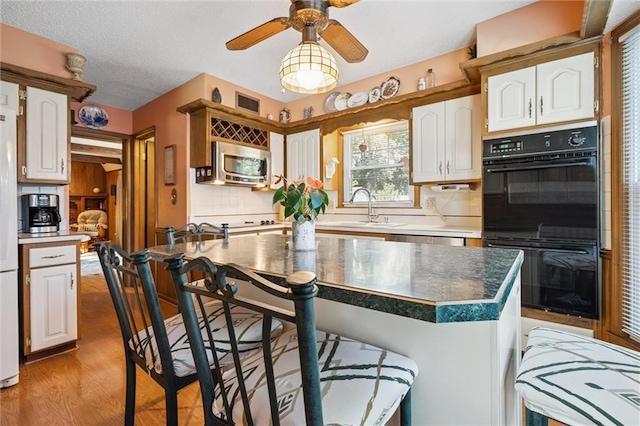 7211 Goodman St, Overland Park, KS 66204 - kitchen with stainless steel microwave, a breakfast bar, decorative backsplash, white cabinetry, and light wood-style flooring