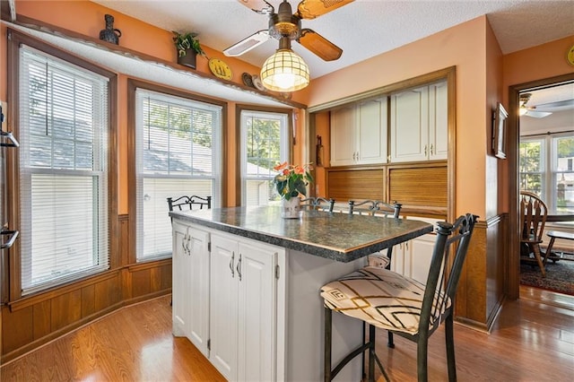 7211 Goodman St, Overland Park, KS 66204 - kitchen with ceiling fan, light wood-style floors, dark countertops, a wainscoted wall, and a breakfast bar area