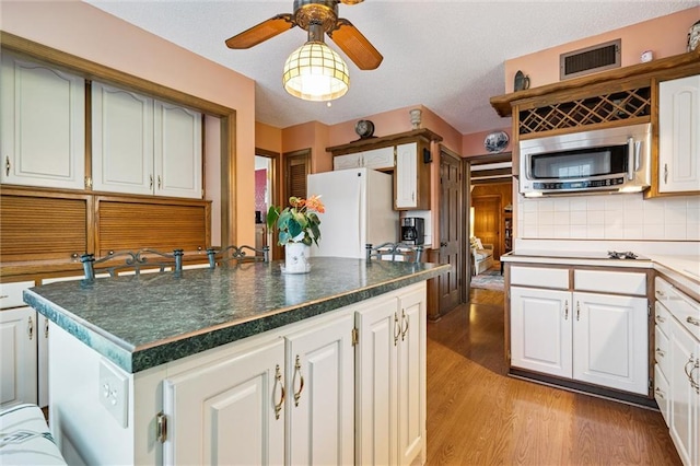 7211 Goodman St, Overland Park, KS 66204 - kitchen featuring stainless steel microwave, freestanding refrigerator, light wood-type flooring, ceiling fan, and white cabinets