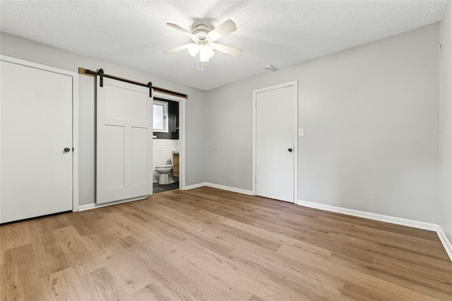 7617 W 63rd Ter, Overland Park, KS 66202 - unfurnished bedroom featuring light wood finished floors, a barn door, a textured ceiling, connected bathroom, and a ceiling fan