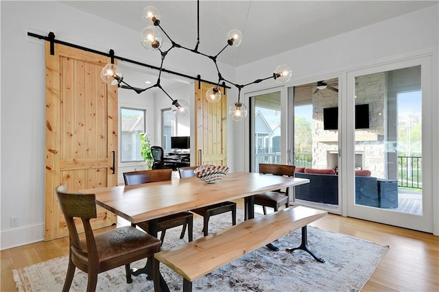 2144 W 89th Ter, Leawood, KS 66206 - dining room with light wood-type flooring, a stone fireplace, a ceiling fan, and a barn door