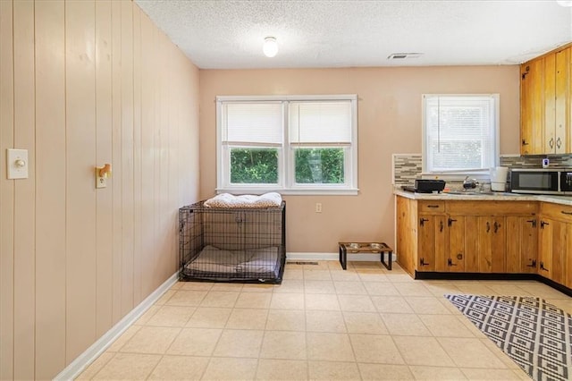 810 Vest Dr, Warrensburg, MO 64093 - kitchen with stainless steel microwave, healthy amount of natural light, light countertops, brown cabinetry, and a textured ceiling