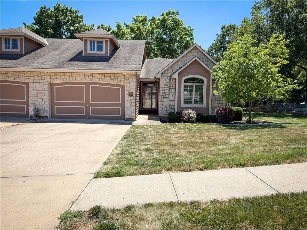 2409 NW Ashurst Dr, Lees Summit, MO 64081 - view of front of house featuring a garage, concrete driveway, a front lawn, stone siding, and roof with shingles