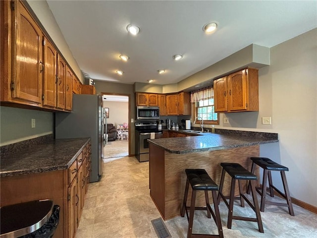 2006 Buckingham St, Saint Joseph, MO 64506 - kitchen featuring stainless steel appliances, a peninsula, brown cabinets, a breakfast bar, and dark countertops