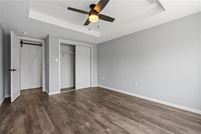 812 W Royle St, Richmond, MO 64085 - unfurnished bedroom with a tray ceiling, dark wood-type flooring, a closet, and a barn door