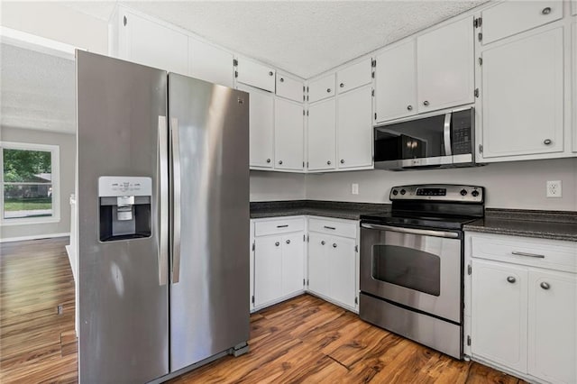 1138 S Willow St, Ottawa, KS 66067 - kitchen featuring stainless steel appliances, a textured ceiling, dark countertops, dark wood finished floors, and white cabinets