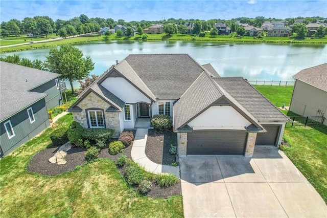 129 SE Chelsea Dr, Lees Summit, MO 64063 - french country home featuring stone siding, an attached garage, driveway, roof with shingles, and a water view