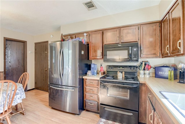 9514 W 77th Ter, Overland Park, KS 66204 - kitchen with range with electric stovetop, black microwave, freestanding refrigerator, light countertops, and light wood finished floors