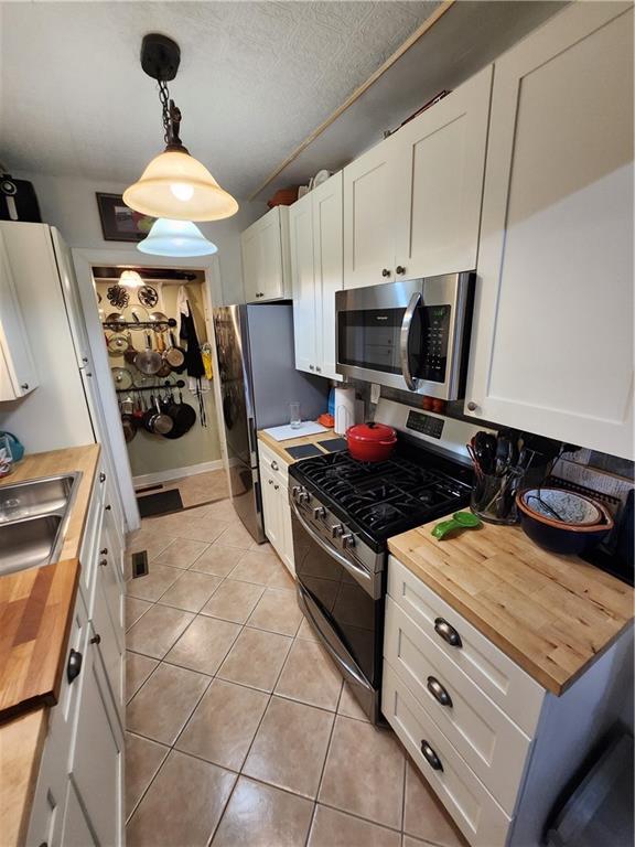 315 N 1st St, Independence, KS 67301 - kitchen featuring butcher block counters, stainless steel appliances, light tile patterned flooring, white cabinets, and decorative light fixtures
