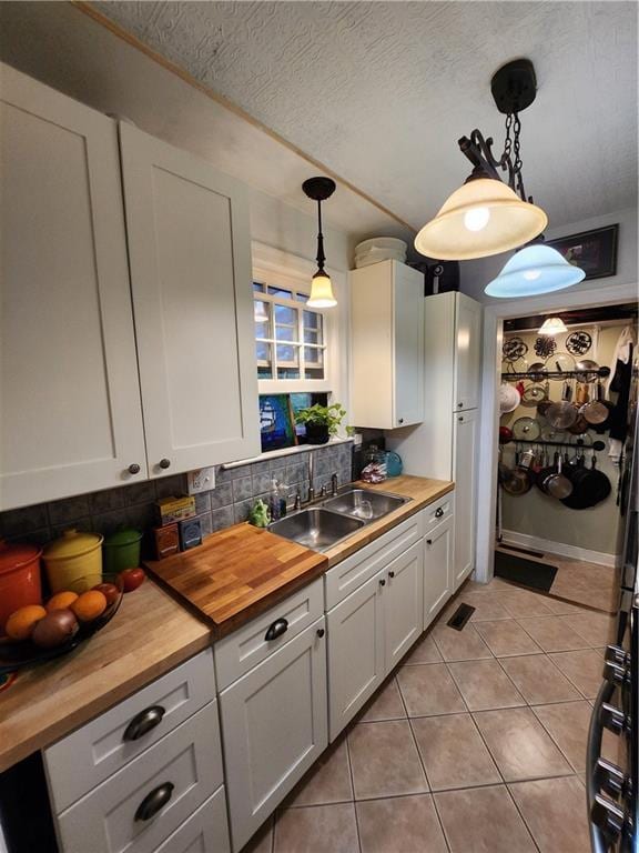 315 N 1st St, Independence, KS 67301 - kitchen featuring butcher block countertops, white cabinets, light tile patterned floors, decorative light fixtures, and a textured ceiling
