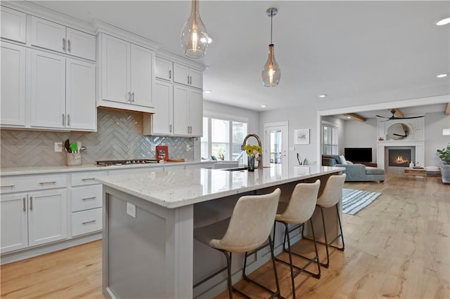 24704 W 76th St, Shawnee, KS 66227 - kitchen featuring light wood-style flooring, tasteful backsplash, light stone counters, white cabinets, and a kitchen island with sink