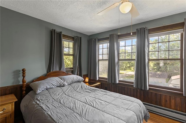 309 E Miami St, Paola, KS 66071 - bedroom featuring a baseboard radiator, a textured ceiling, wood walls, and a ceiling fan