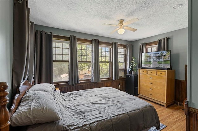 309 E Miami St, Paola, KS 66071 - bedroom featuring a textured ceiling, light wood-style floors, a wainscoted wall, and a ceiling fan