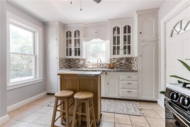 521 Tracy Ave, Kansas City, MO 64016 - kitchen featuring light tile patterned floors, a kitchen island, backsplash, electric stove, and white cabinetry