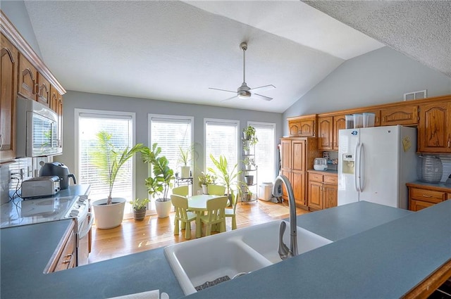 3945 N 123rd Ter, Kansas City, KS 66109 - kitchen featuring white refrigerator with ice dispenser, stainless steel microwave, a ceiling fan, vaulted ceiling, and wood finished floors