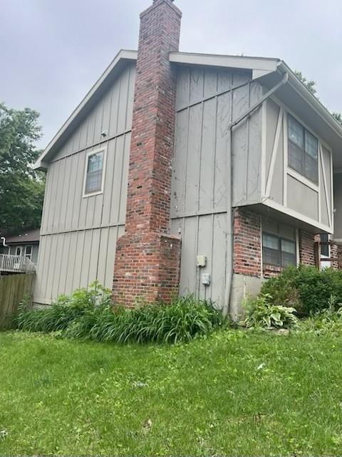 10195 Haskins St, Lenexa, KS 66217 - view of home's exterior with board and batten siding, a chimney, brick siding, and a lawn