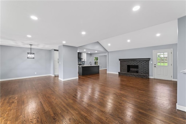 9916 Floyd St, Overland Park, KS 66212 - unfurnished living room with vaulted ceiling, a brick fireplace, dark wood-style flooring, and recessed lighting