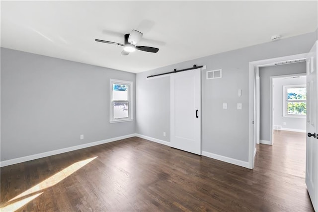 9916 Floyd St, Overland Park, KS 66212 - unfurnished bedroom with a barn door, multiple windows, dark wood-style flooring, and ceiling fan