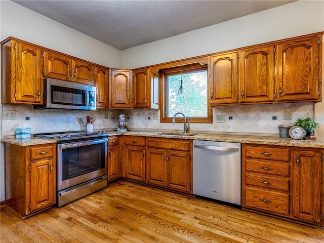 28804 E 116th St, Lees Summit, MO 64086 - kitchen featuring appliances with stainless steel finishes, brown cabinetry, light wood-type flooring, decorative backsplash, and a textured ceiling