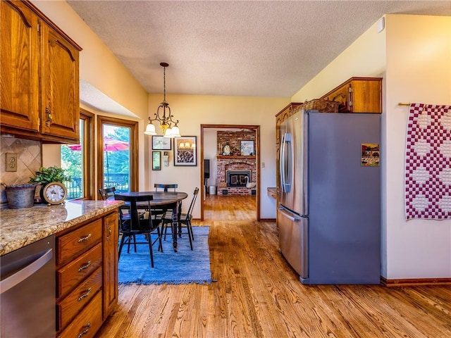 28804 E 116th St, Lees Summit, MO 64086 - kitchen featuring stainless steel appliances, light wood-style floors, a textured ceiling, decorative light fixtures, and brown cabinetry