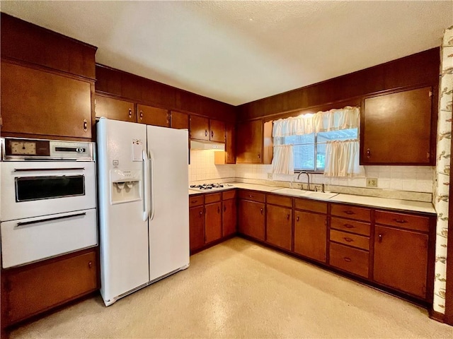 15007 E 41st St, Independence, MO 64055 - kitchen featuring white appliances, light countertops, decorative backsplash, under cabinet range hood, and brown cabinetry