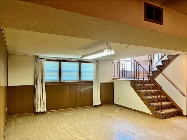 15007 E 41st St, Independence, MO 64055 - unfurnished room with tile patterned floors, stairs, wainscoting, wooden walls, and healthy amount of natural light