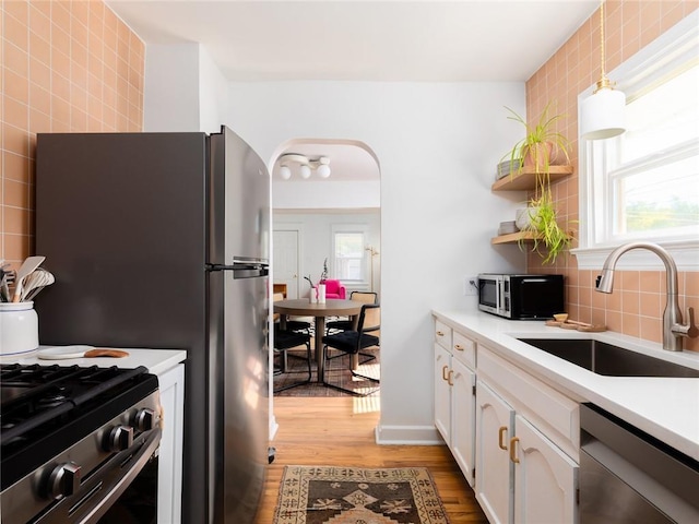 4206 Mission Rd, Kansas City, KS 66103 - kitchen featuring appliances with stainless steel finishes, light wood finished floors, white cabinetry, arched walkways, and light countertops