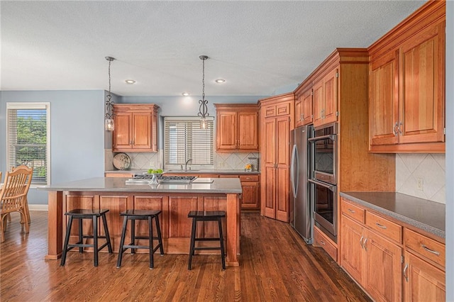 14622 S Garnett St, Olathe, KS 66062 - kitchen featuring dark wood-style floors, a breakfast bar, stainless steel appliances, a center island, and brown cabinets