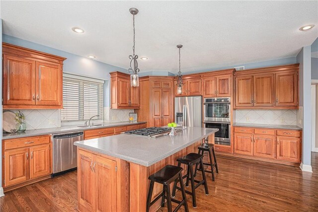 14622 S Garnett St, Olathe, KS 66062 - kitchen featuring appliances with stainless steel finishes, a kitchen island, brown cabinetry, dark wood-type flooring, and recessed lighting