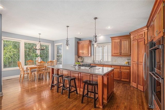 14622 S Garnett St, Olathe, KS 66062 - kitchen featuring stainless steel gas stovetop, dark wood-style flooring, tasteful backsplash, brown cabinets, and a breakfast bar area
