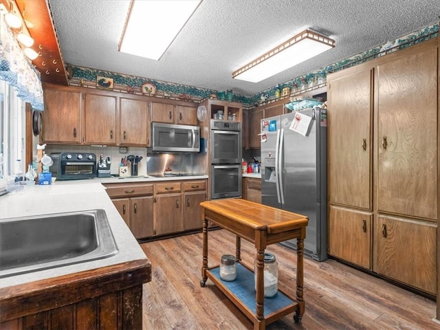 1490 216th St, Lathrop, MO 64465 - kitchen featuring appliances with stainless steel finishes, light wood finished floors, light countertops, a textured ceiling, and brown cabinetry