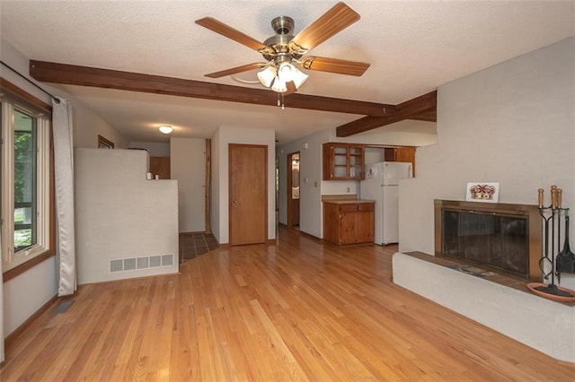 918 King St, Baldwin City, KS 66006 - unfurnished living room featuring light wood-style flooring, beam ceiling, a glass covered fireplace, a ceiling fan, and a textured ceiling