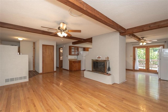 918 King St, Baldwin City, KS 66006 - unfurnished living room with ceiling fan, light wood-style floors, beam ceiling, a textured ceiling, and a glass covered fireplace
