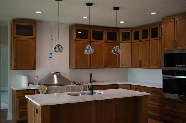 12820 N Arbor Way, Platte City, MO 64079 - kitchen featuring appliances with stainless steel finishes, brown cabinets, glass insert cabinets, an island with sink, and hanging light fixtures