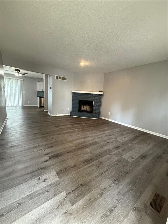 401-07 NE Highland Ln, Blue Springs, MO 64014 - unfurnished living room featuring a textured ceiling, a brick fireplace, dark wood finished floors, and ceiling fan