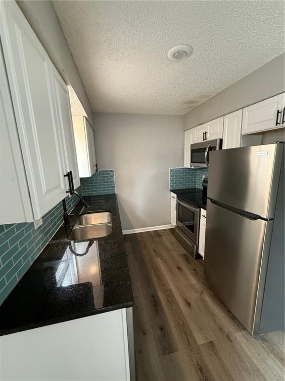 401-07 NE Highland Ln, Blue Springs, MO 64014 - kitchen with appliances with stainless steel finishes, a textured ceiling, white cabinets, decorative backsplash, and dark countertops