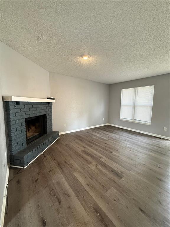 401-07 NE Highland Ln, Blue Springs, MO 64014 - unfurnished living room with wood finished floors, a textured ceiling, and a brick fireplace