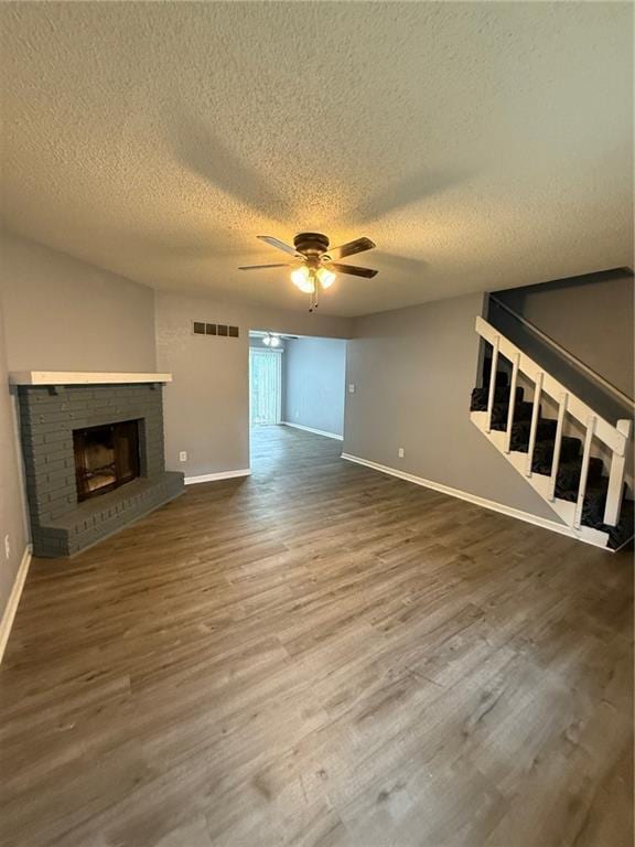 401-07 NE Highland Ln, Blue Springs, MO 64014 - unfurnished living room with a ceiling fan, wood finished floors, a textured ceiling, a fireplace, and stairway