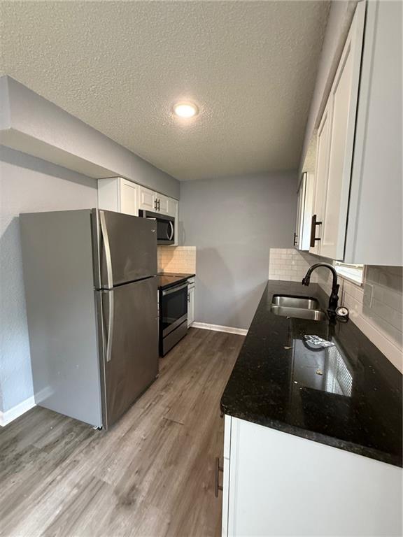 401-07 NE Highland Ln, Blue Springs, MO 64014 - kitchen with appliances with stainless steel finishes, a textured ceiling, white cabinets, wood finished floors, and backsplash