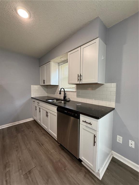 401-07 NE Highland Ln, Blue Springs, MO 64014 - kitchen featuring stainless steel dishwasher, a textured ceiling, dark wood-style flooring, dark countertops, and tasteful backsplash