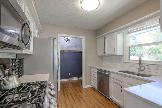 1921 SW 4th St, Lees Summit, MO 64081 - kitchen with appliances with stainless steel finishes, a textured ceiling, light wood-style floors, white cabinetry, and light countertops