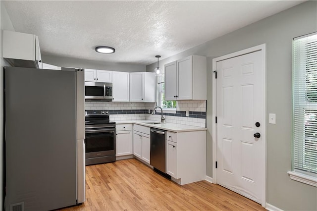 1304 E 41st St, Kansas City, MO 64110 - kitchen featuring stainless steel appliances, decorative backsplash, light wood-style floors, light countertops, and a textured ceiling