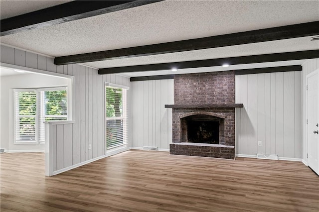 16620 E 36th St, Independence, MO 64055 - unfurnished living room with wood finished floors, beam ceiling, a textured ceiling, a brick fireplace, and wooden walls