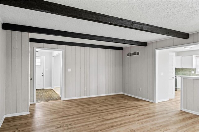 16620 E 36th St, Independence, MO 64055 - unfurnished living room with beamed ceiling, light wood finished floors, a textured ceiling, and wood walls