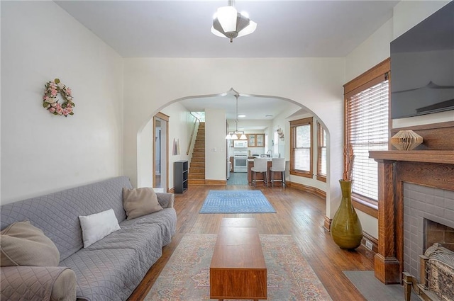 3923 Campbell St, Kansas City, MO 64110 - living room featuring arched walkways, stairs, wood finished floors, and a fireplace with flush hearth