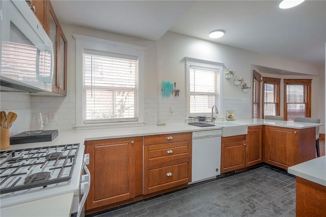3923 Campbell St, Kansas City, MO 64110 - kitchen featuring white appliances, a peninsula, brown cabinetry, light countertops, and backsplash