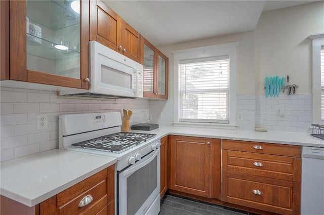 3923 Campbell St, Kansas City, MO 64110 - kitchen with white appliances, brown cabinetry, decorative backsplash, glass insert cabinets, and light countertops
